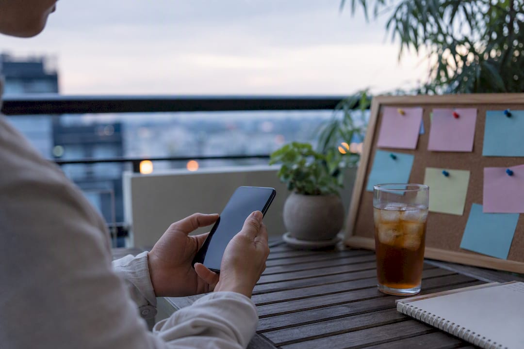 Hands holding smartphone near whiteboard and plant